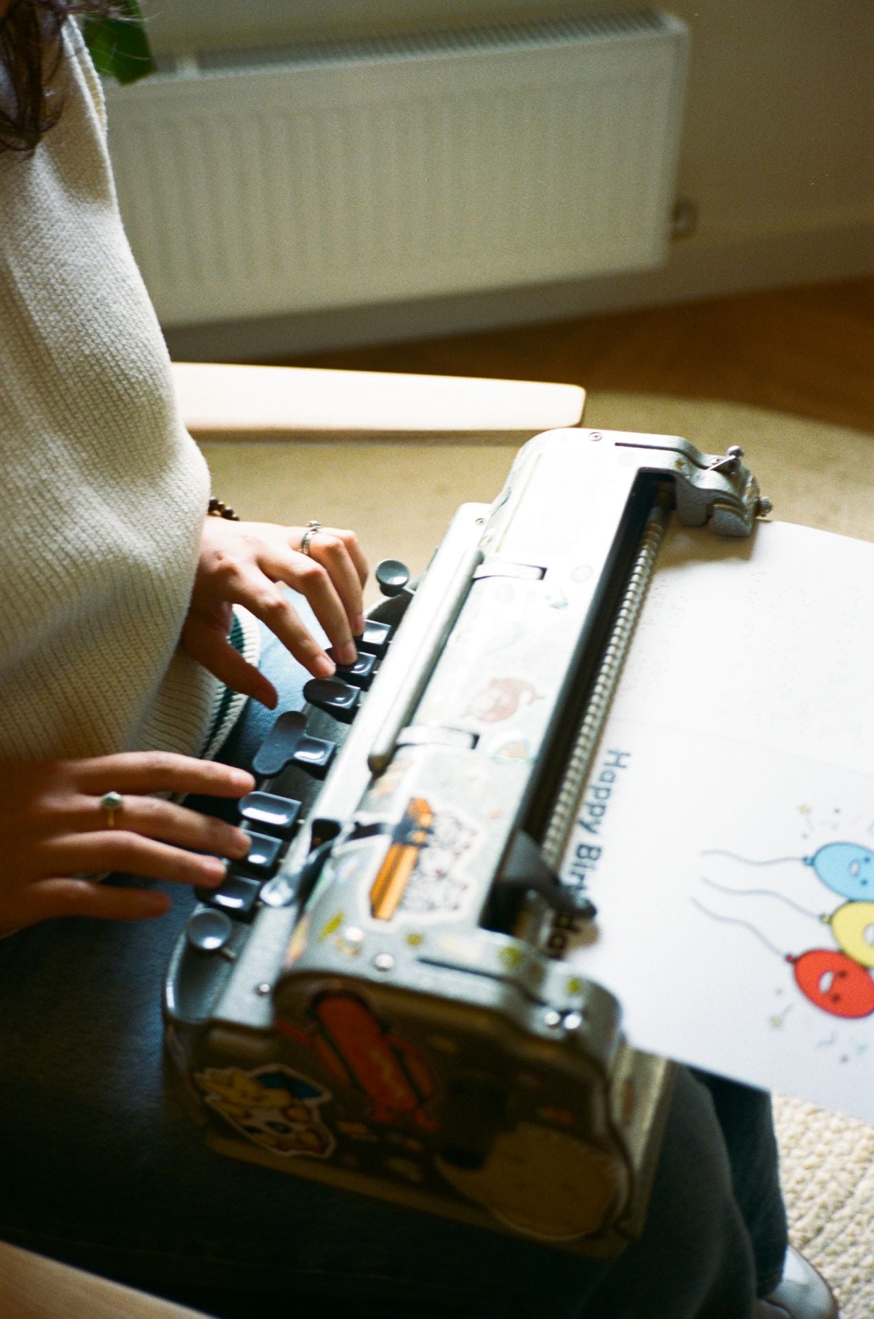 Person typing on a Perkins Brailler with a colorful birthday card in the feed roller. Someone is brailling on the card.