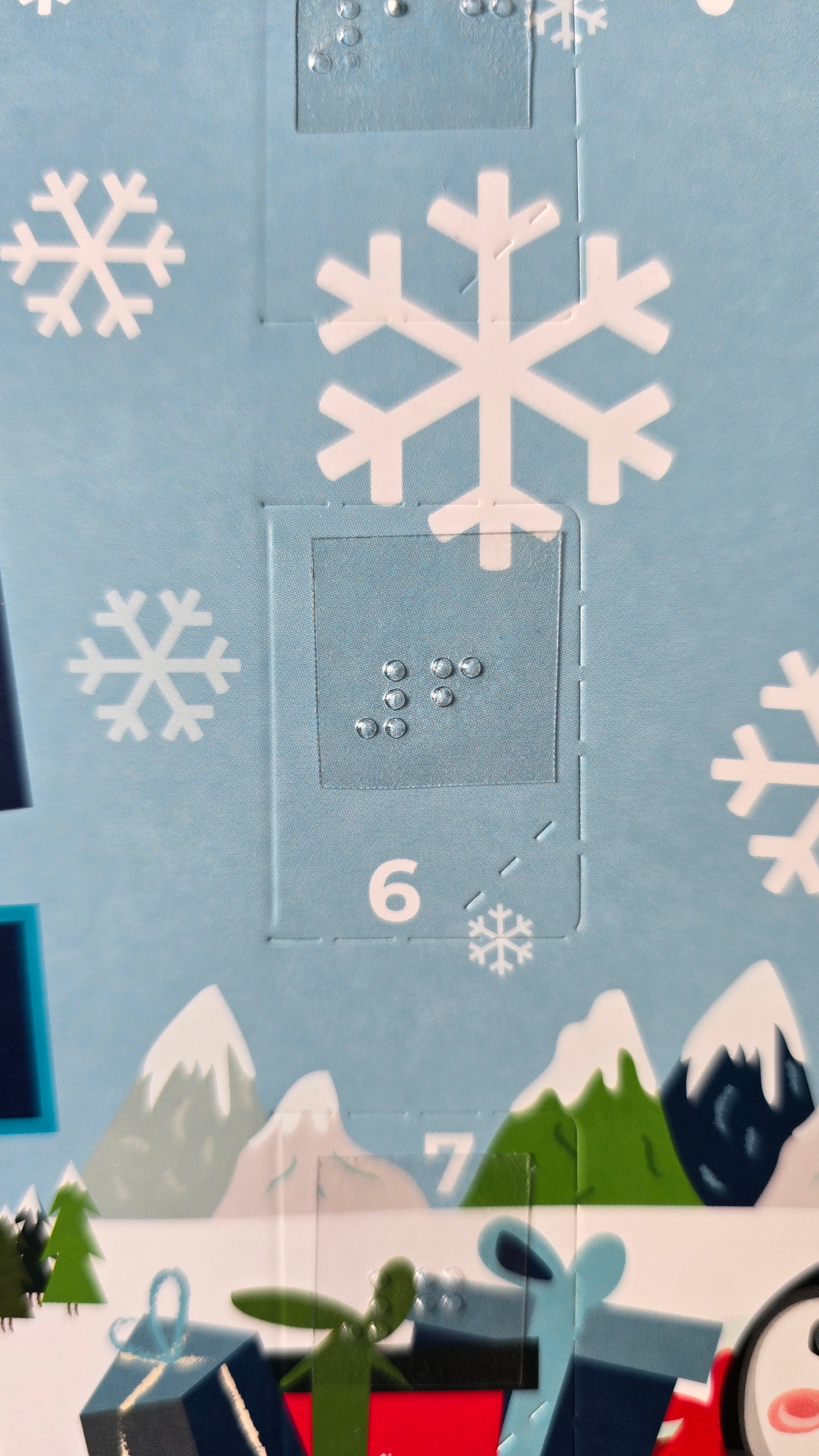 Close-up of a Christmas-themed advent calendar with snowflakes and a blue background. There is braille placed over the number 6 on the Advent calendar.