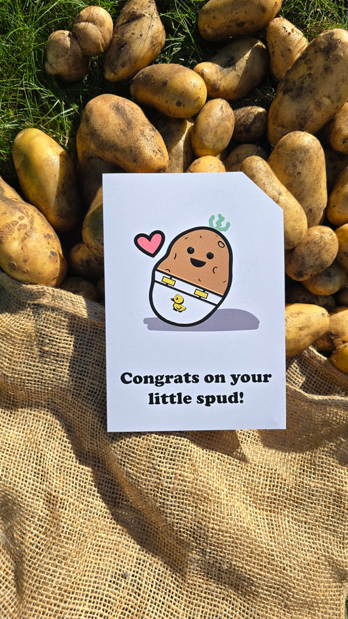 Card front with a smiling, cartoon potato character wearing a nappy/diaper with a duck on it. There is a small pink heart next to the potato. The text on the bottom reads 'Congrats on your little spud!', in bold black letters. The top right hand corner is cut off, for orientation purposes. A unique Dot & Type feature.
The image is of the card lay on a hessian sack which has potatoes falling out of it.