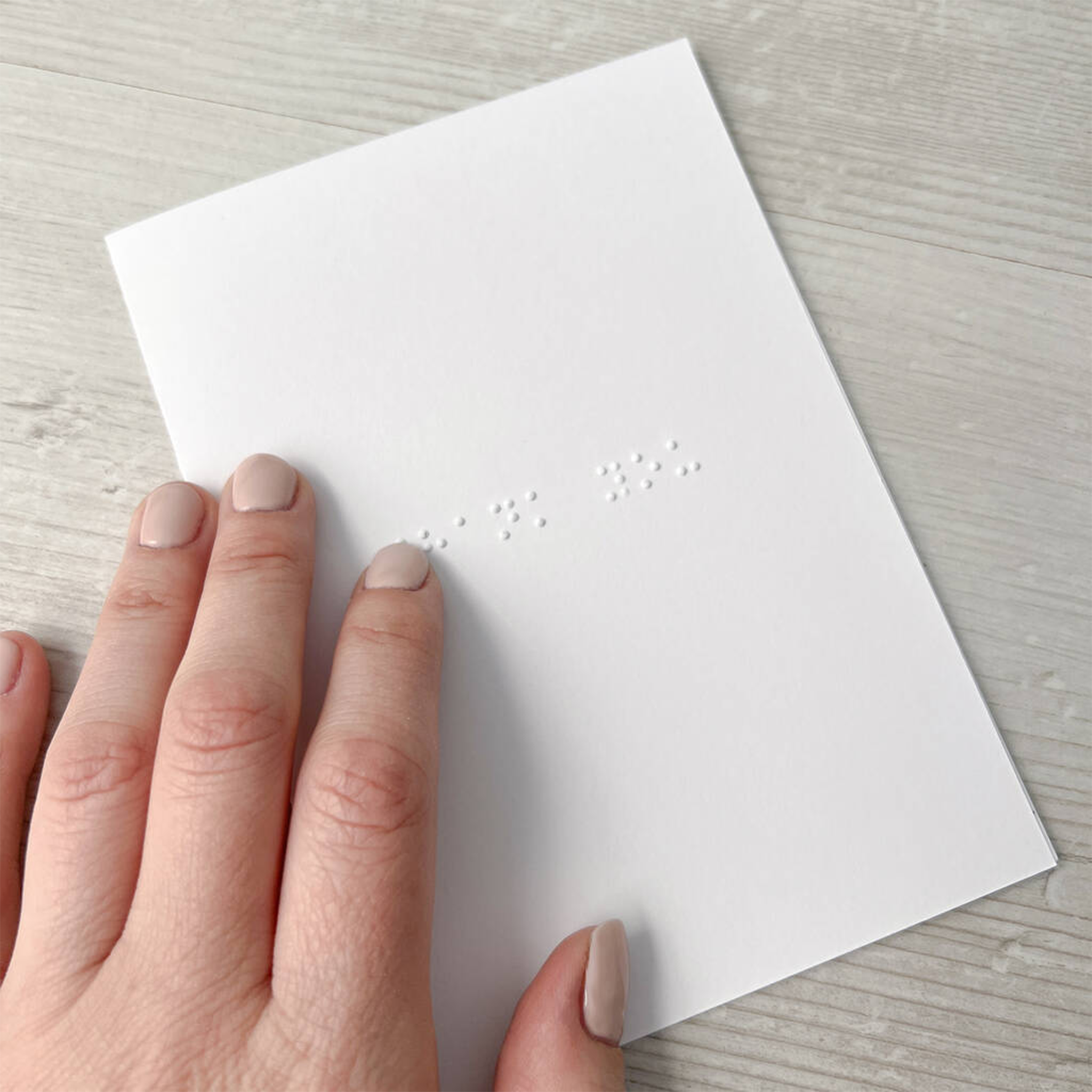 Hand holding a white card with braille text on a light wooden surface